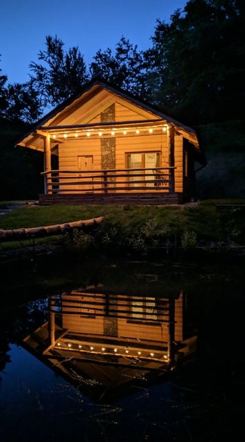 Klimatycznie oświetlony domek wieczorową porą - odbicie w tafli wody.