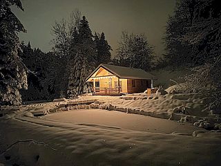 Bieszczady - Domek nad stawem - nocne zdjęcie domku z promieniami światła wylatującego przez okna.
